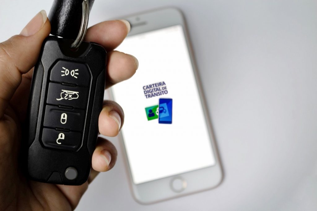 pessoa segurando chave de carro; ao fundo, celular aberto com aplicativo da CNH Digital