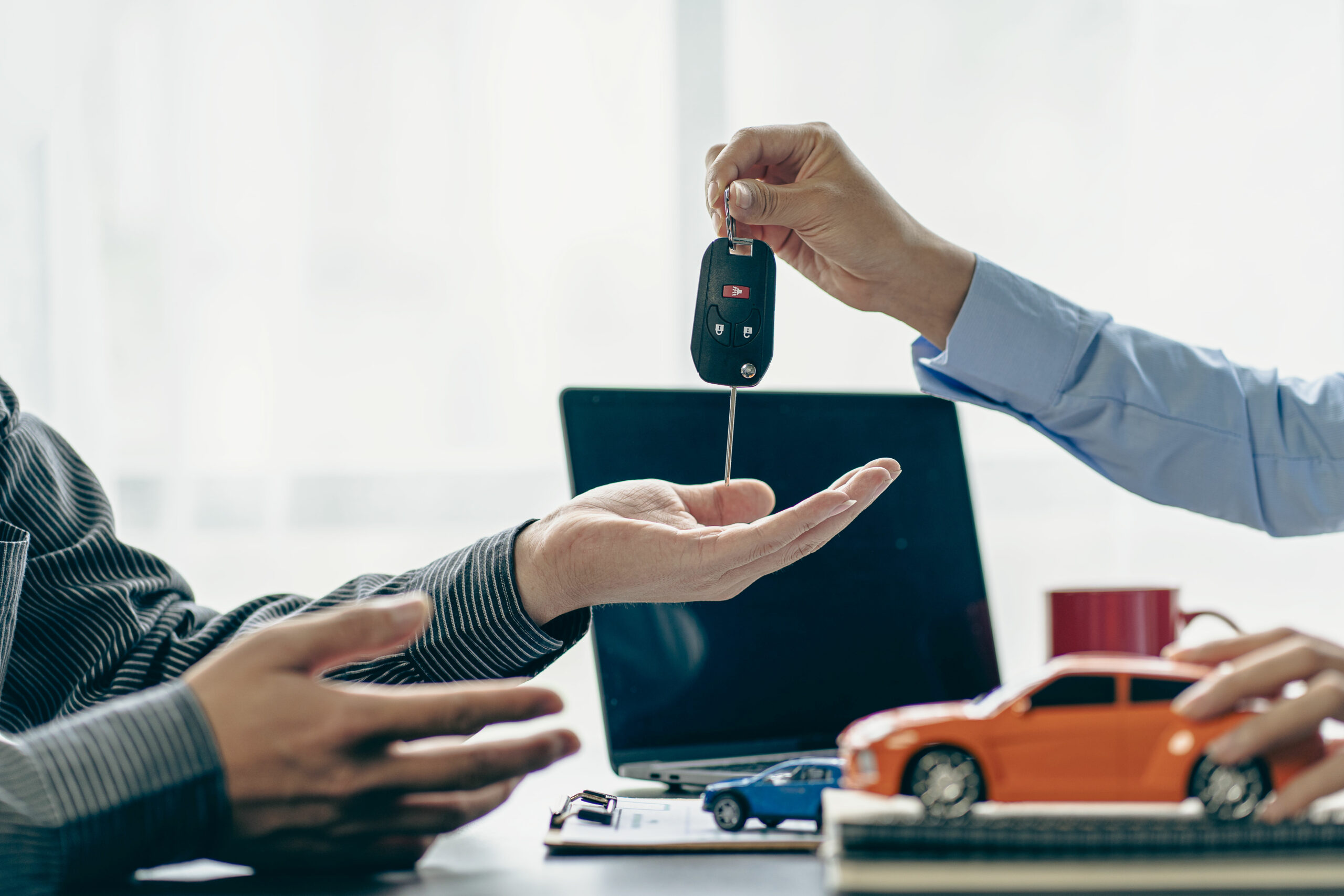 Mão entregando chave de carro para outra mão com miniatura de carro ao lado